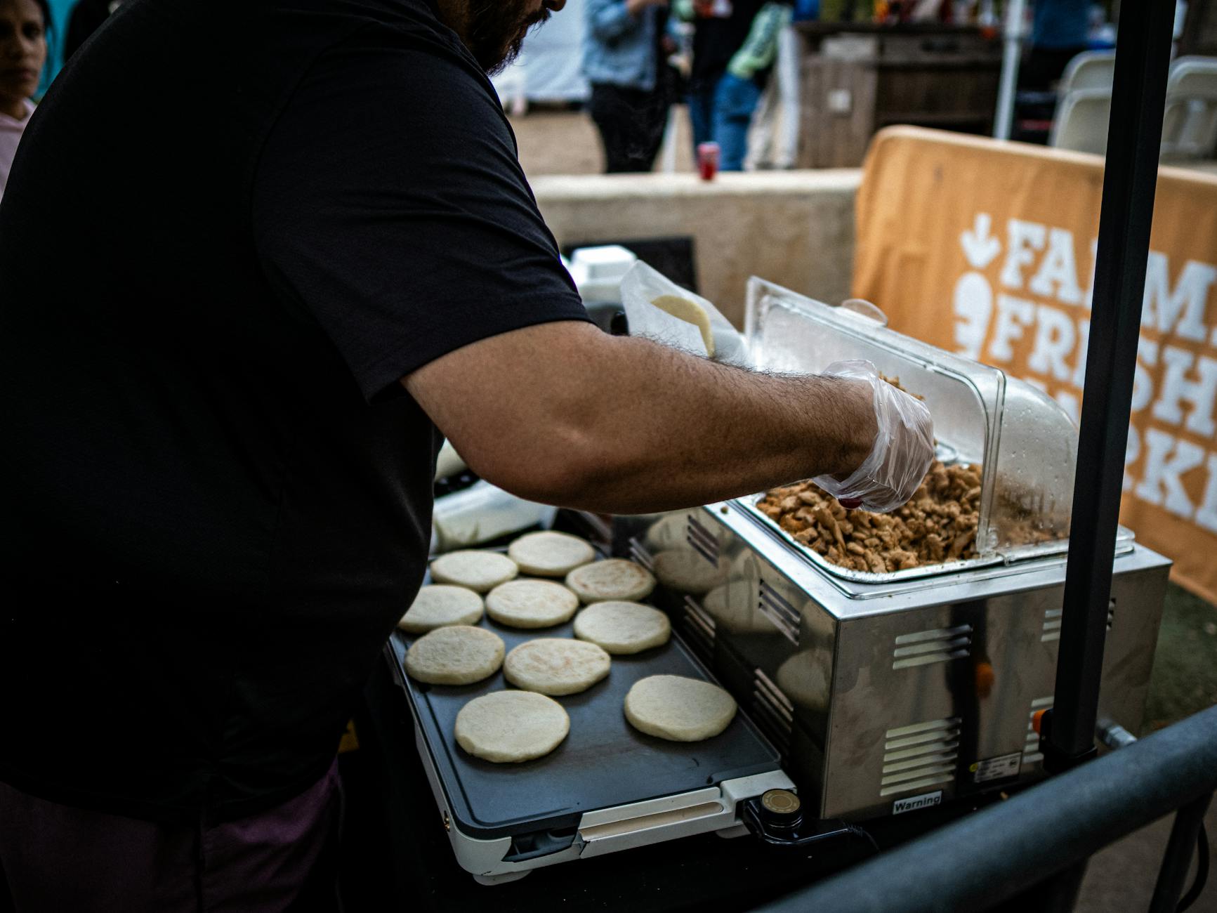 Kolumbijski uliczny sprzedawca smaży arepy z mięsnym farszem na targu