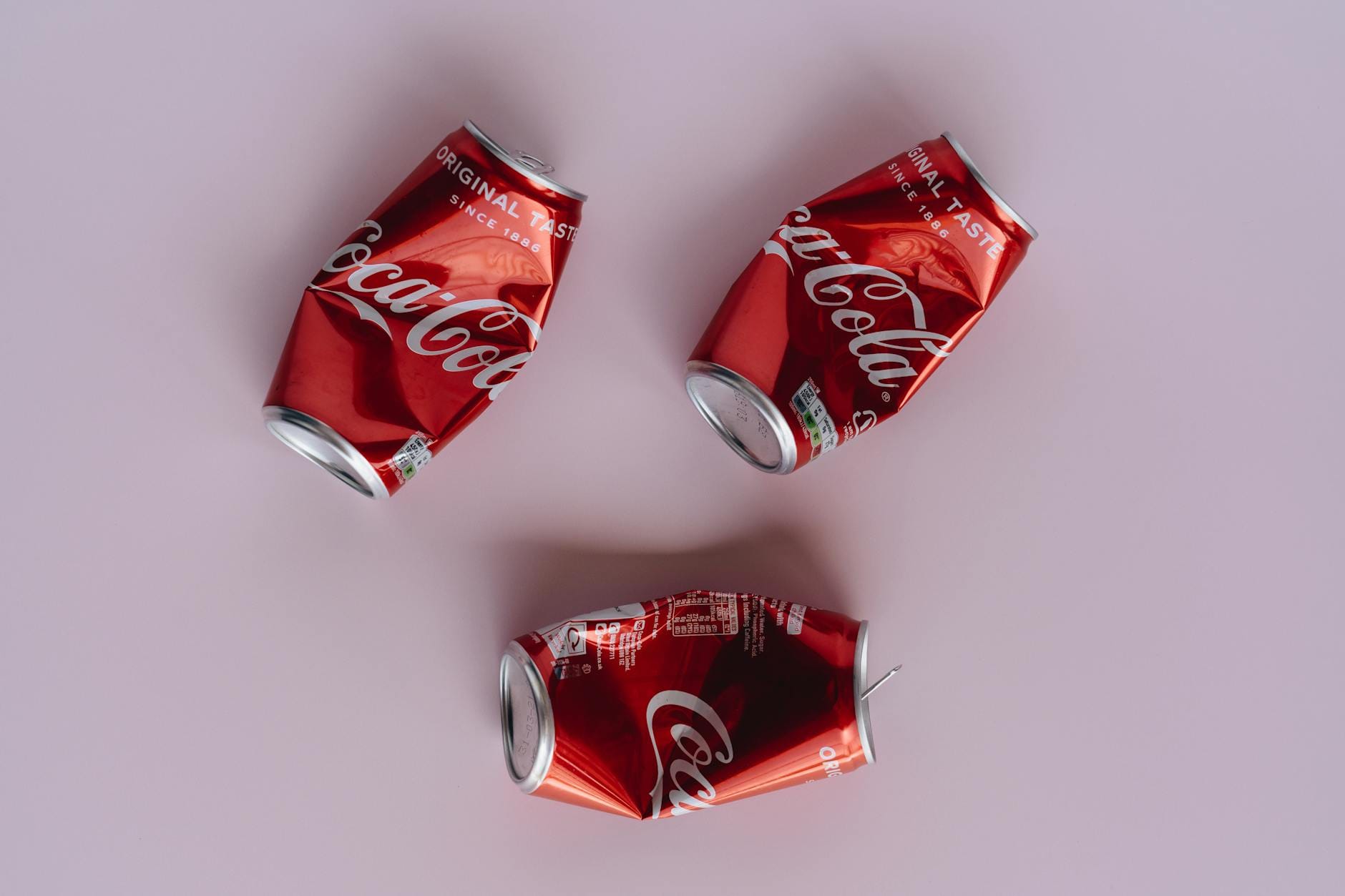 Pogniecione puszki Coca-Coli na różowym tle, symbol recyklingu w przemyśle