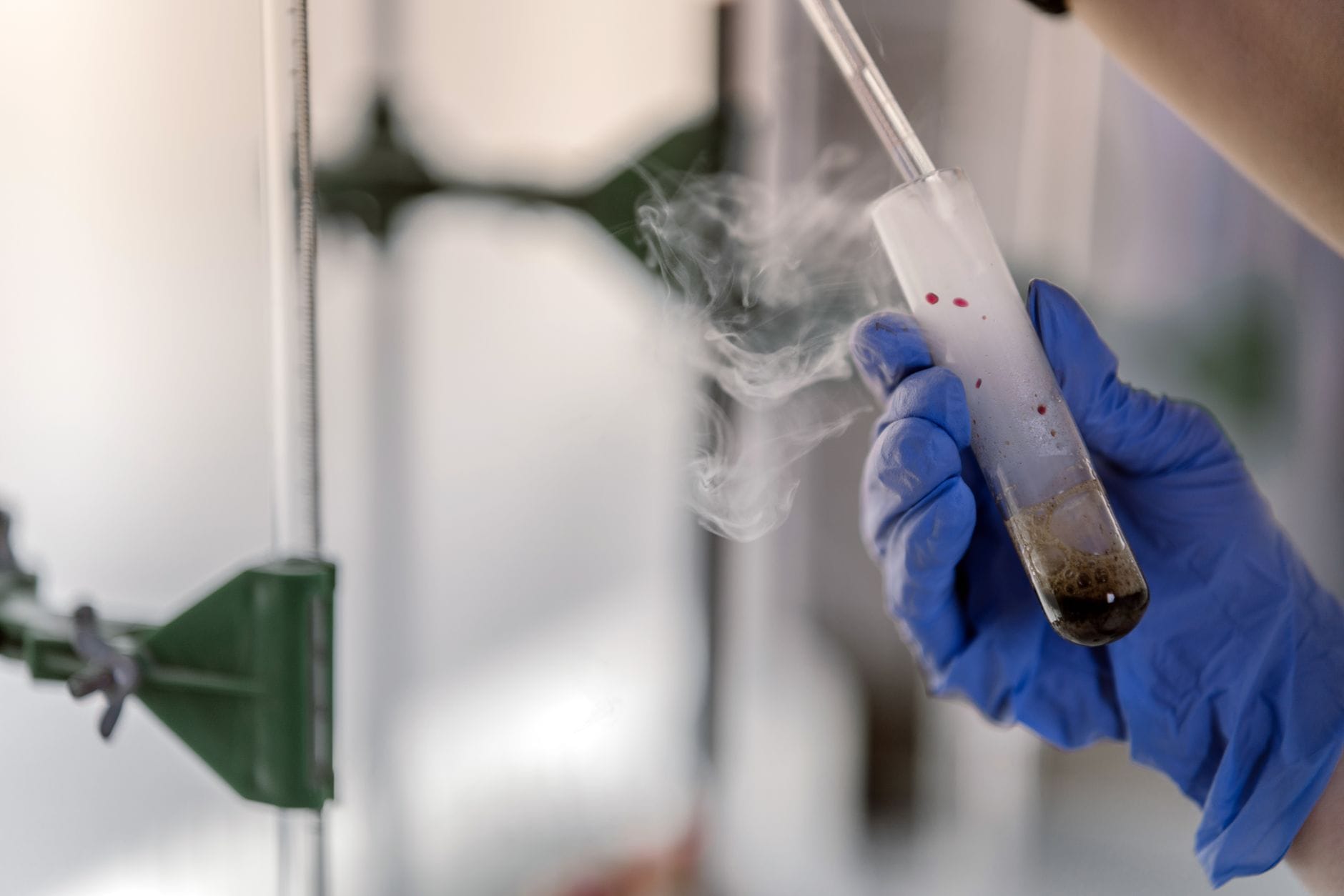 Ręka w rękawiczce trzyma parującą probówkę w laboratorium